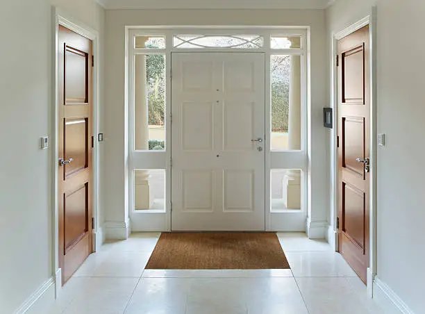 White paneled front door with glass sidelites and transom in a bright foyer