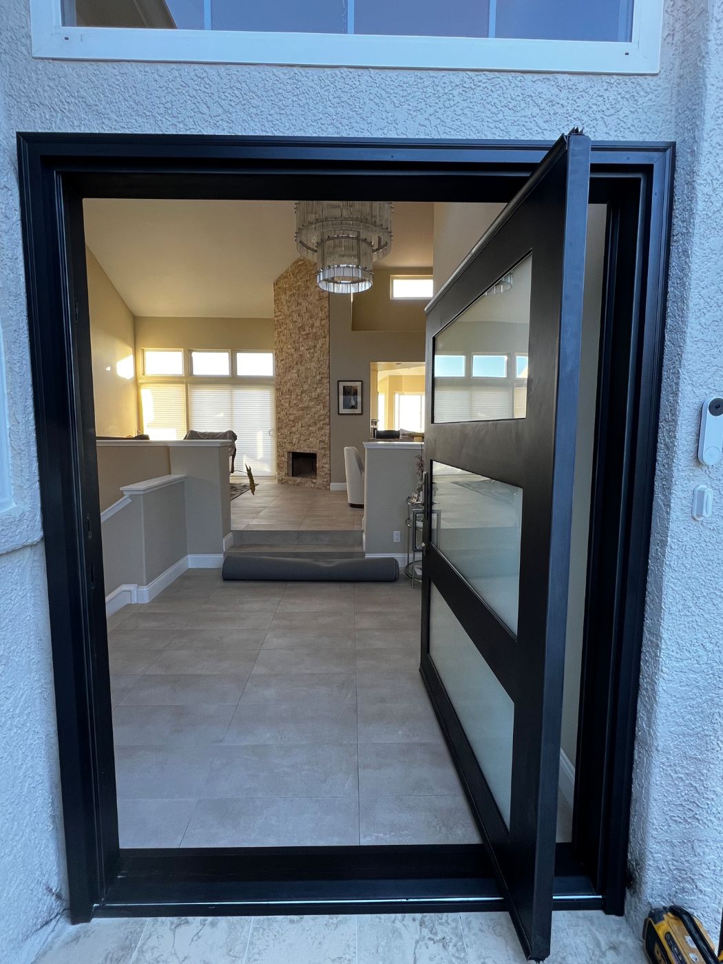 Black pivot entry door with frosted glass panels, open to a bright living room