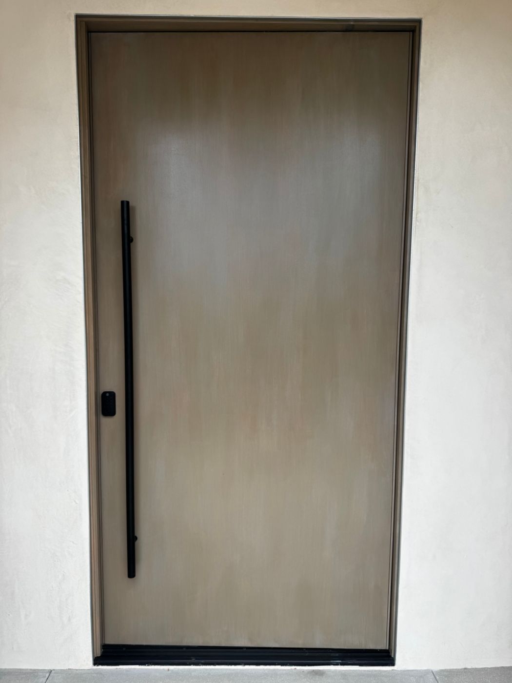 Flush wood-veneer pivot door with full-height black pull and keypad lock