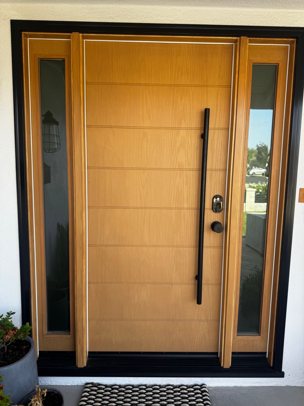 Modern wood-grain entry door with black pull handle and glass sidelites