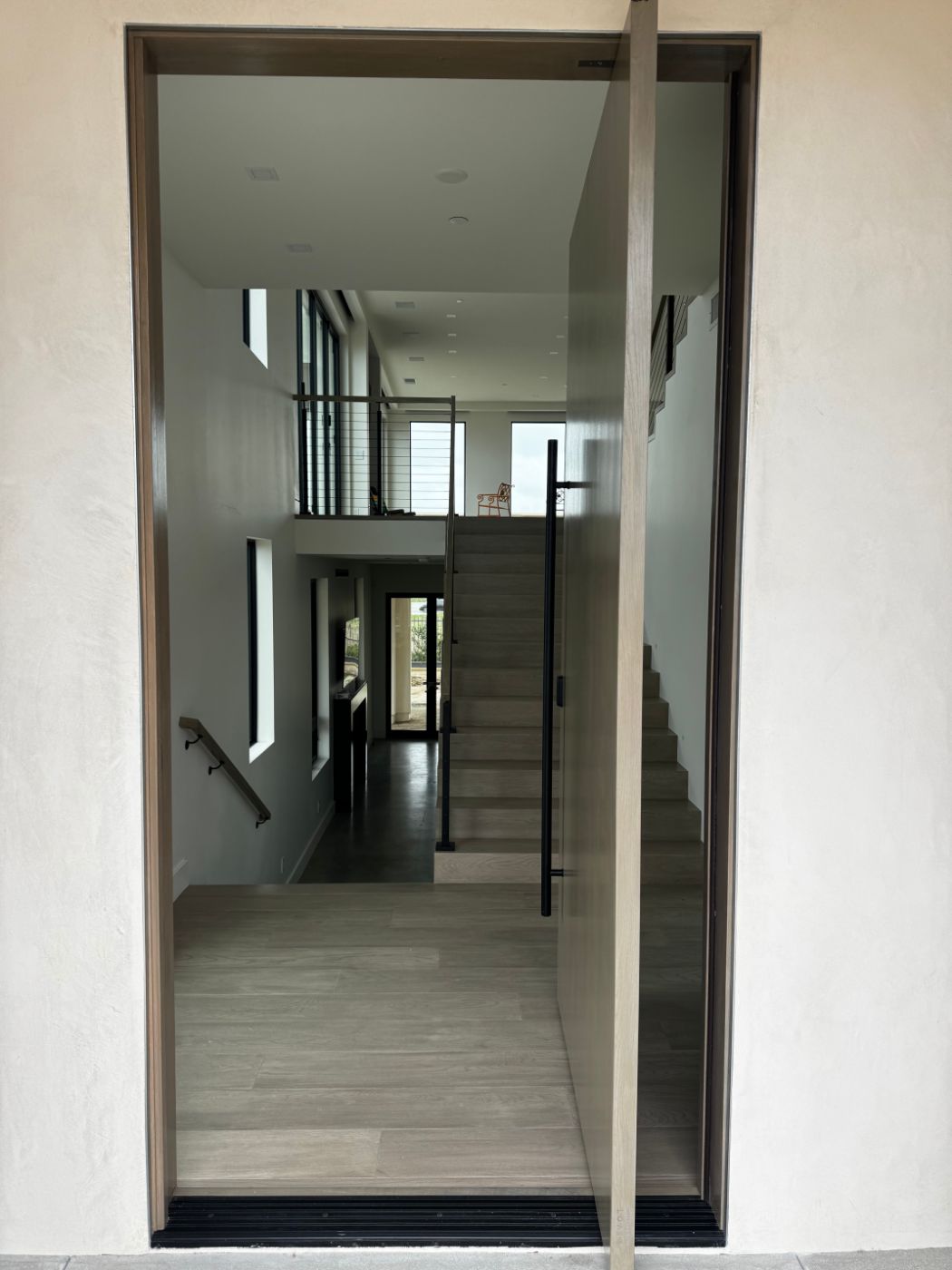 Oversized oak pivot door opening into a modern two-story entry