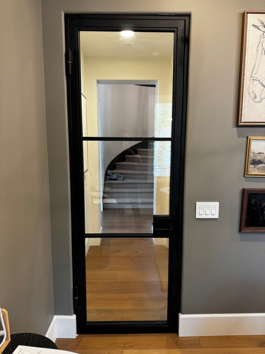 Black steel-framed interior glass door looking toward a curved staircase