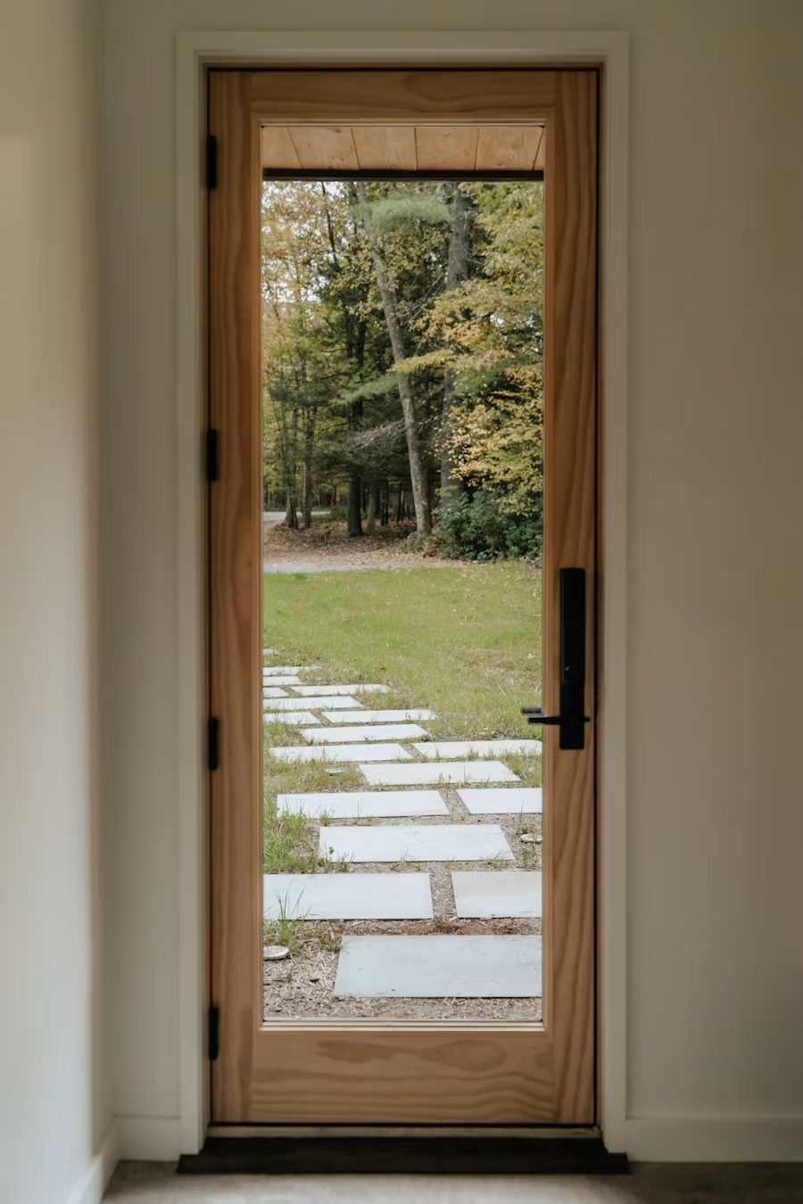 Natural wood full-glass door looking out to a stone path and trees